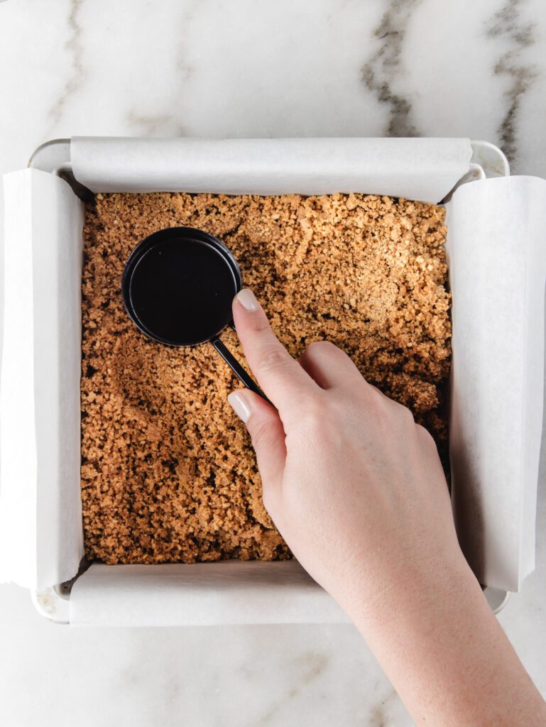 Patting cookie crumbs into bottom of cake tin.