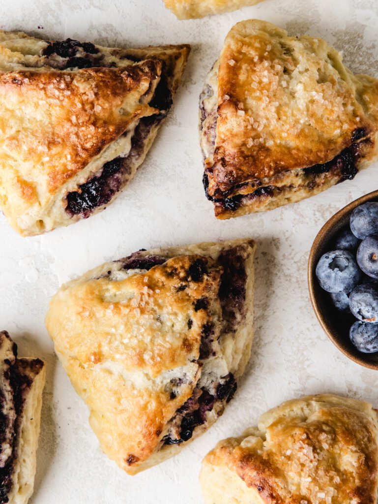 Scones scattered on marble with blueberries.